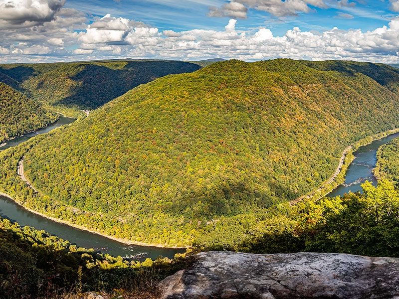 Aerial view of New River Gorge with lush green hills and winding river.